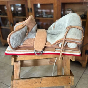 Montura de competición con cama de lana El Carpincho vista lateral sobre caballo de madera.